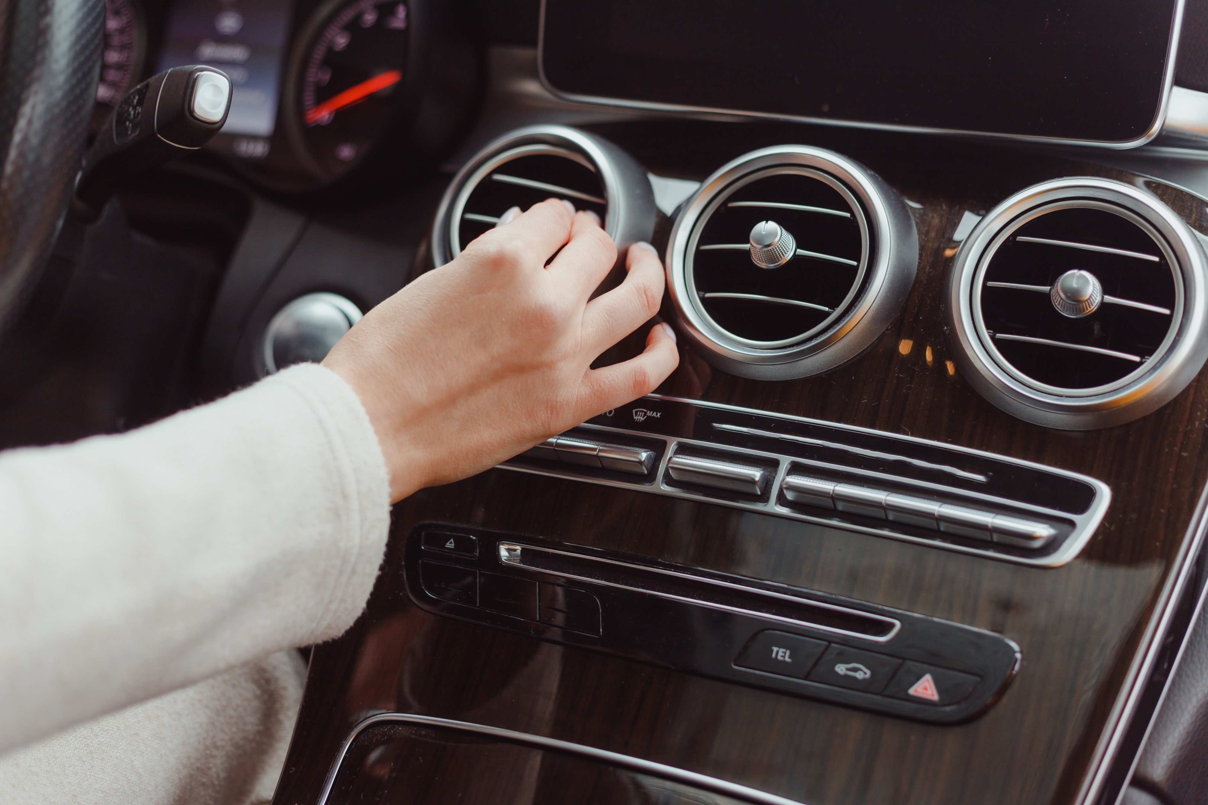 Hand adjusting the round air conditioning vents on the car's dashboard
