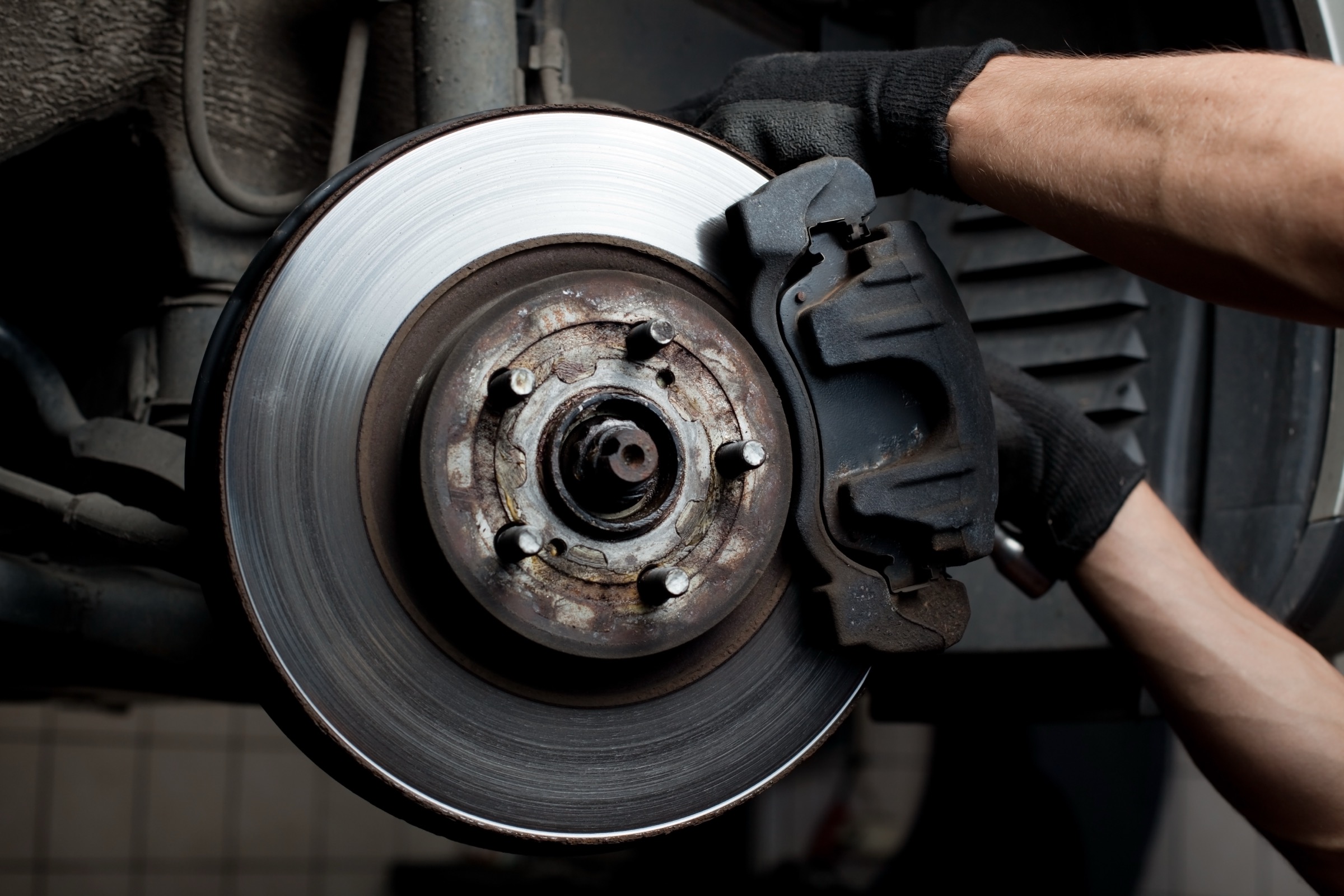 Mechanic in a work glove fitting the brake caliper onto a brake disc on a vehicle